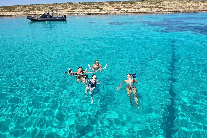 People swimming in clear blue water with a boat in the background. 1