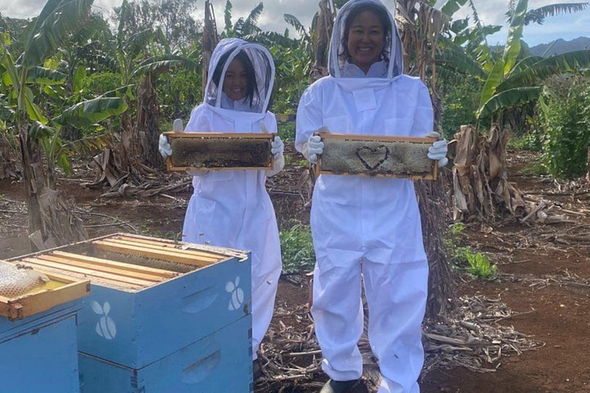 Zwei Personen in weißen Schutzanzügen halten einen Bienenstockrahmen. 4