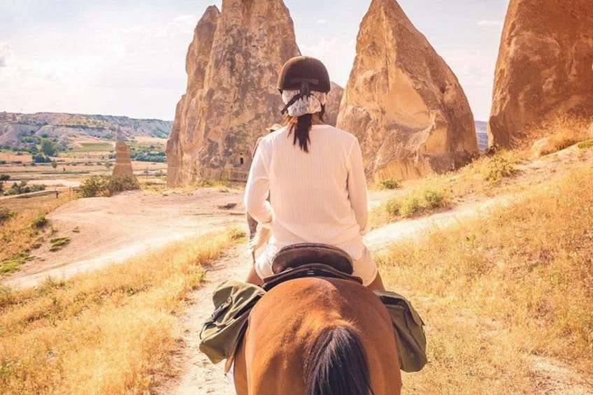 Una persona monta a caballo por un sendero de tierra con grandes formaciones rocosas al fondo. 5