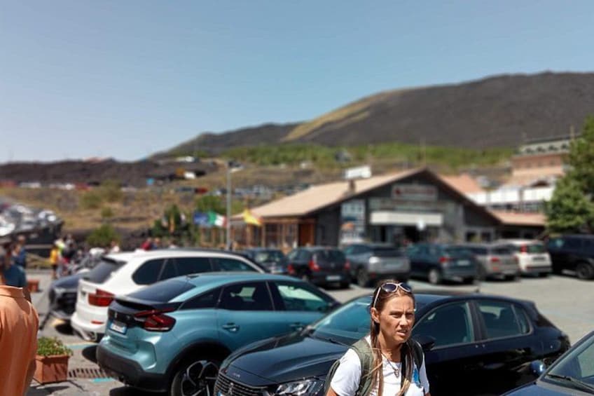 Ein Parkplatz mit Autos, ein Gebäude mit einem Schild und eine hügelige Landschaft im Hintergrund. 4