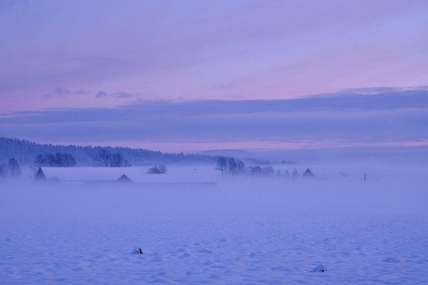 A snowy landscape with a few buildings and trees under a purple sky. 3