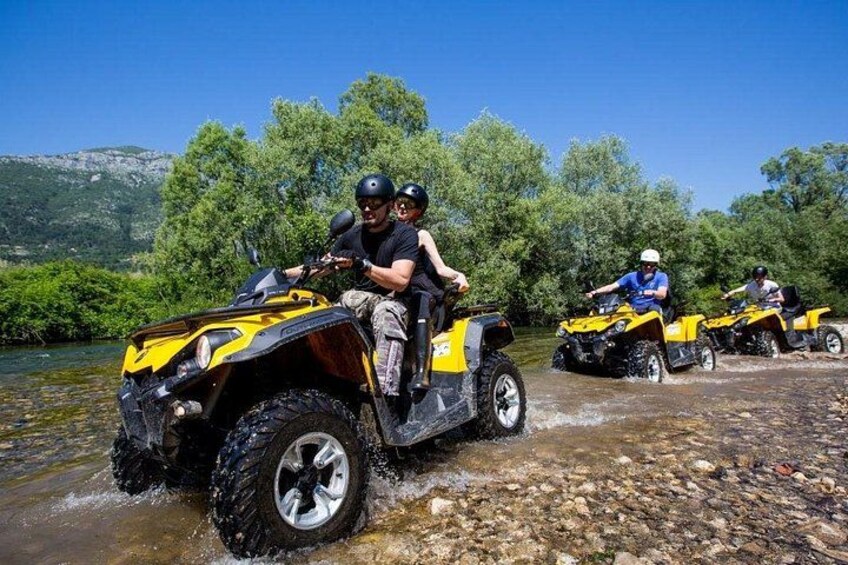 Three people riding yellow all-terrain vehicles (ATVs) on a rocky riverbed. 2