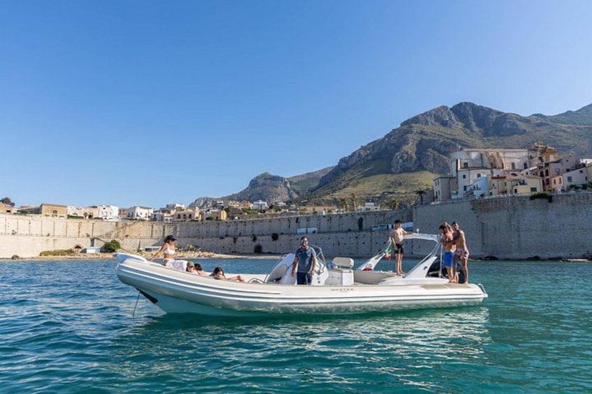 Un motoscafo bianco con persone a bordo vicino a una località costiera con un muro di pietra e edifici. 3