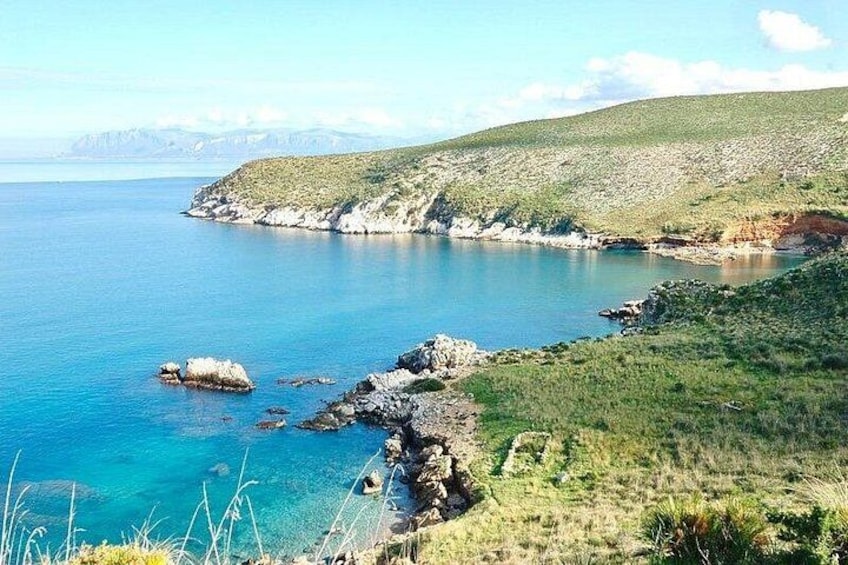 A coastal landscape with clear blue waters, rocky shores, and grassy hills. 4