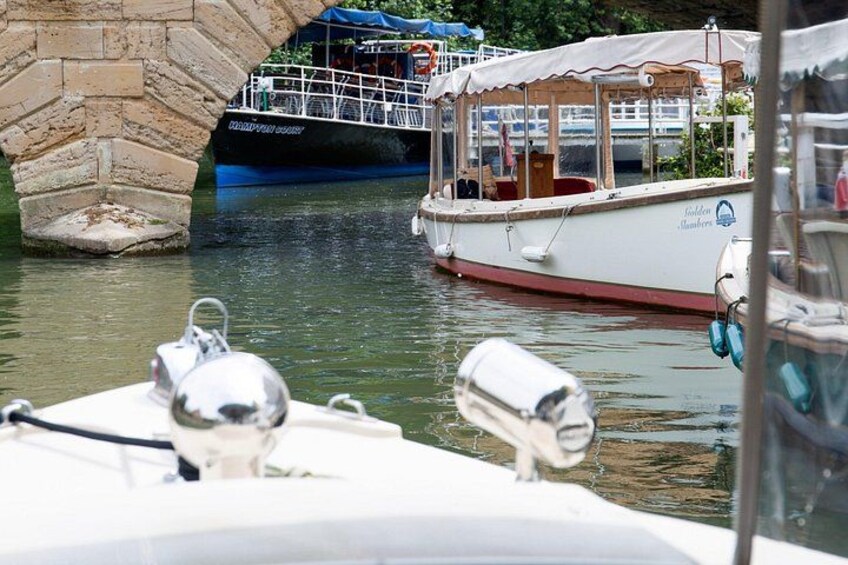 A canal with boats, a stone bridge, and a covered boat with a white and red hull. 1