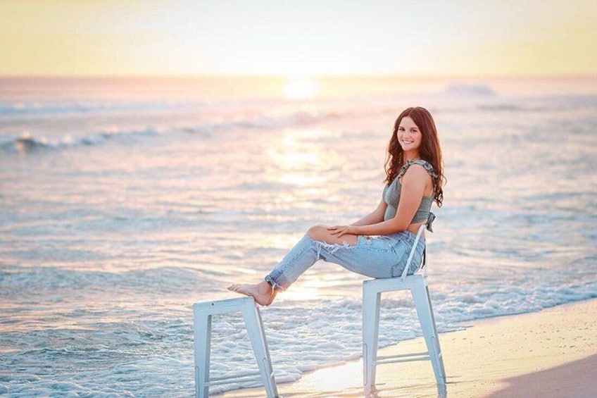 A person sitting on a white stool by the ocean during sunset. 1