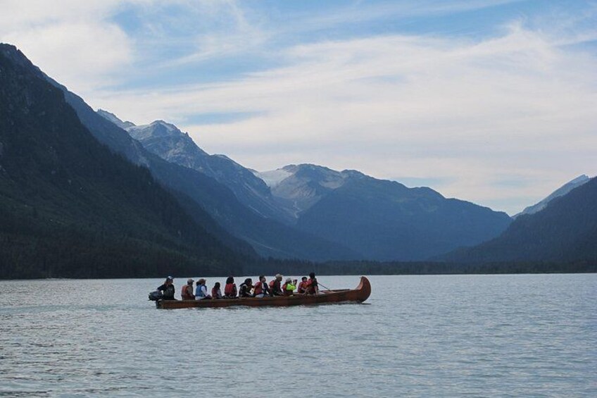 A group of people in a canoe on a calm lake surrounded by mountains. 1