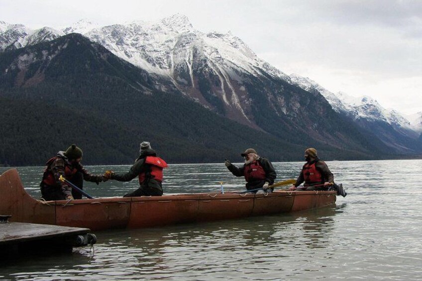 Four people in a canoe on a calm lake with snow-capped mountains in the background. 2