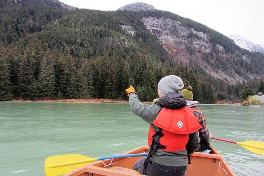 A person in a boat wearing a life jacket, pointing towards the shore. 3