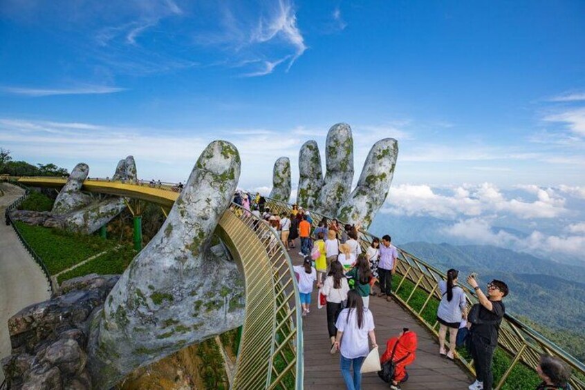 Un gruppo di persone su una passeggiata con grandi sculture di pietra a forma di mano, con vista su un paesaggio montuoso. 2