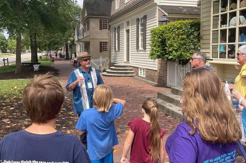 Un groupe de personnes se tient devant un bâtiment historique, avec un chemin pavé de briques et des arbres. 1