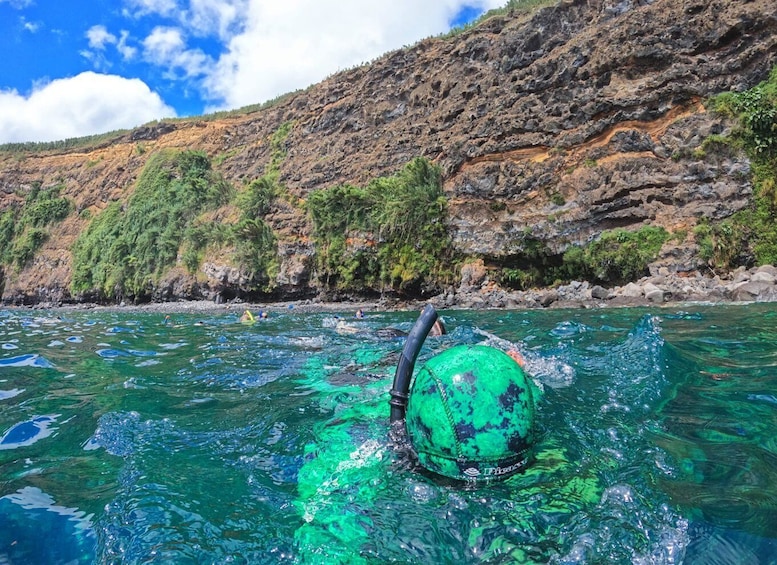 Un juguete inflable verde en aguas transparentes, con una ladera rocosa al fondo. 3