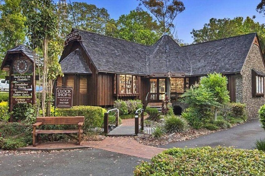 A rustic building with a clock, a sign for a clock shop, and a wooden bench. 2