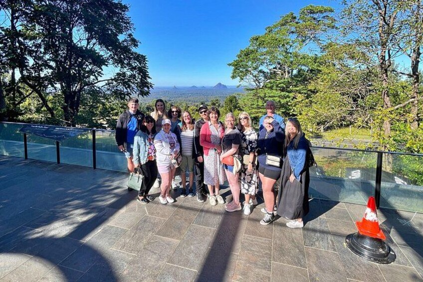 A group of people standing on a paved area with a scenic view of trees and mountains in the background. 3