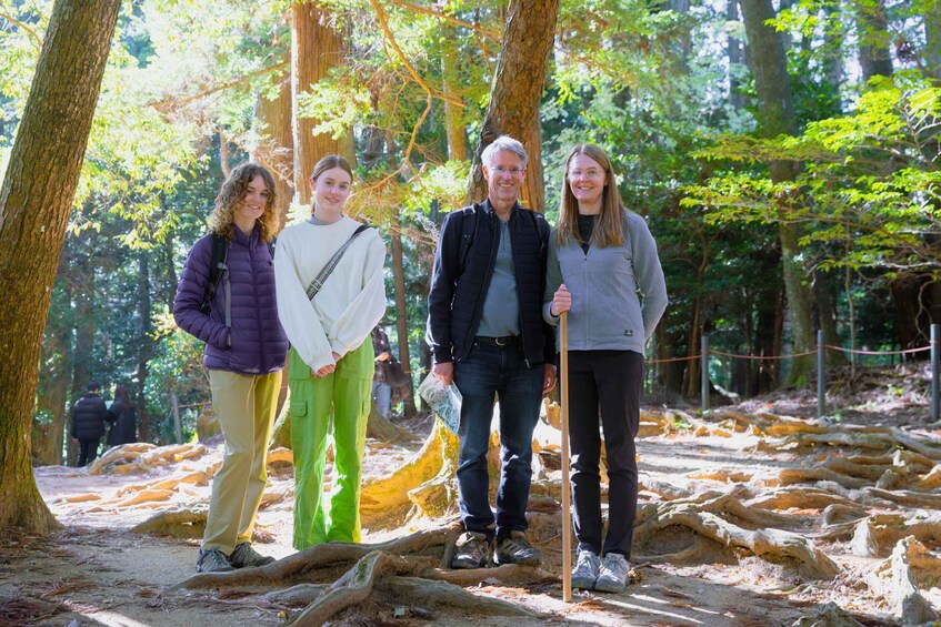 A group of people standing on a forest trail with trees and fallen leaves. 1