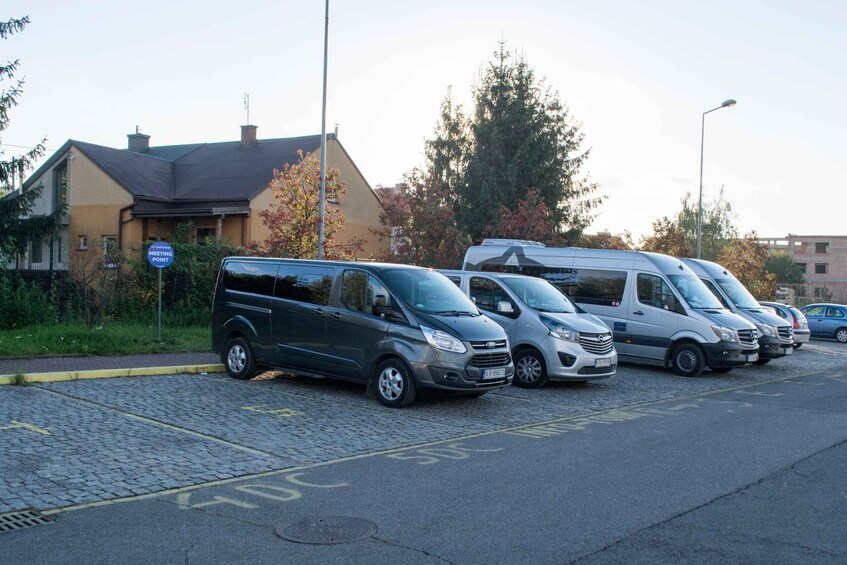 A row of parked vans and a camper van on a cobblestone street with a 'No Parking' sign and a 'Meeting Point' sign. 3
