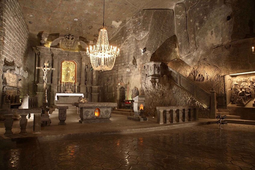 A dimly lit, historic church interior with a large chandelier, stone walls, and religious statues. 1