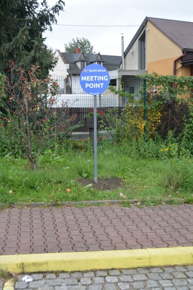 A sign labeled "Meeting Point" with a blue background and white text, surrounded by greenery and a building in the background. 4