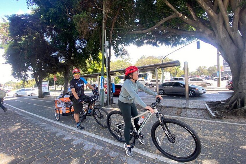 En person som cyklar på en asfalterad stig, en annan person med en cykel och en parkerad bil. 4