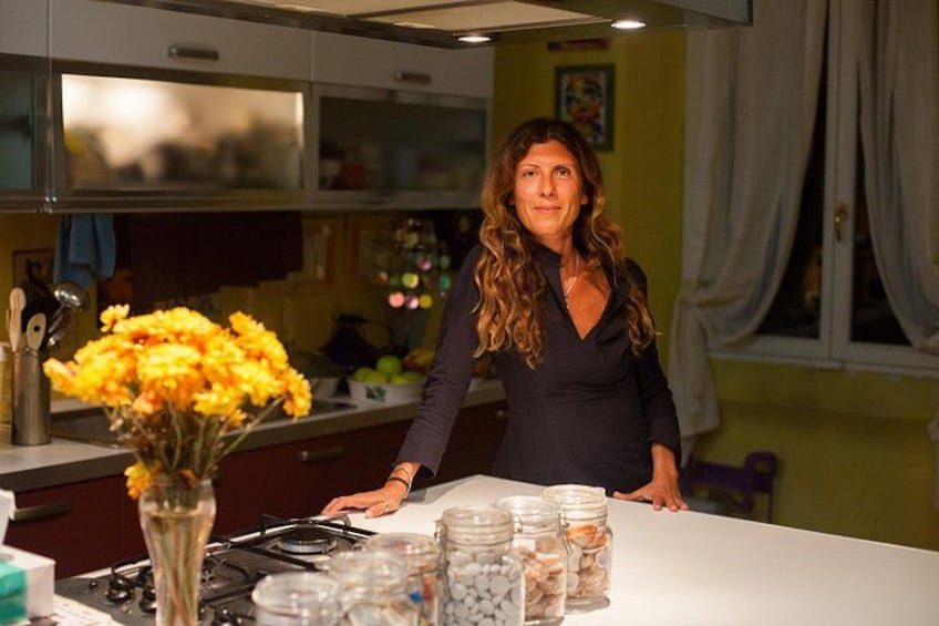 Una mujer en una cocina con una encimera blanca, frascos y un jarrón con flores. 1