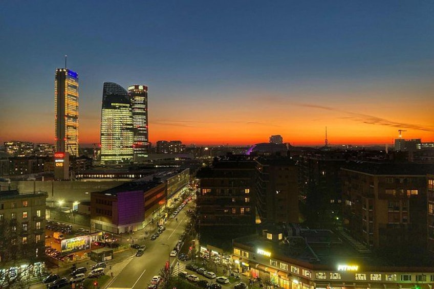 Un paisaje urbano al atardecer con edificios iluminados y una calle concurrida. 4