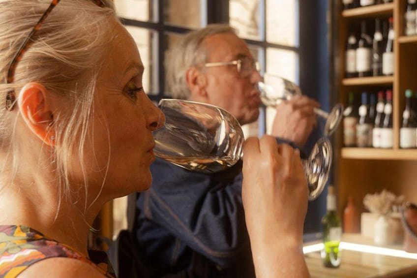 A person holding a wine glass, another person in the background, and a shelf with bottles. 2