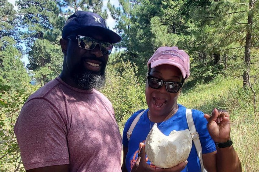 Two people in a forested area, one holding a large white object. 1