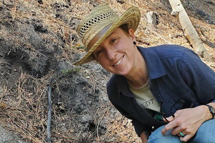 A person wearing a straw hat and a dark shirt, sitting on the ground with a watch on their wrist. 2