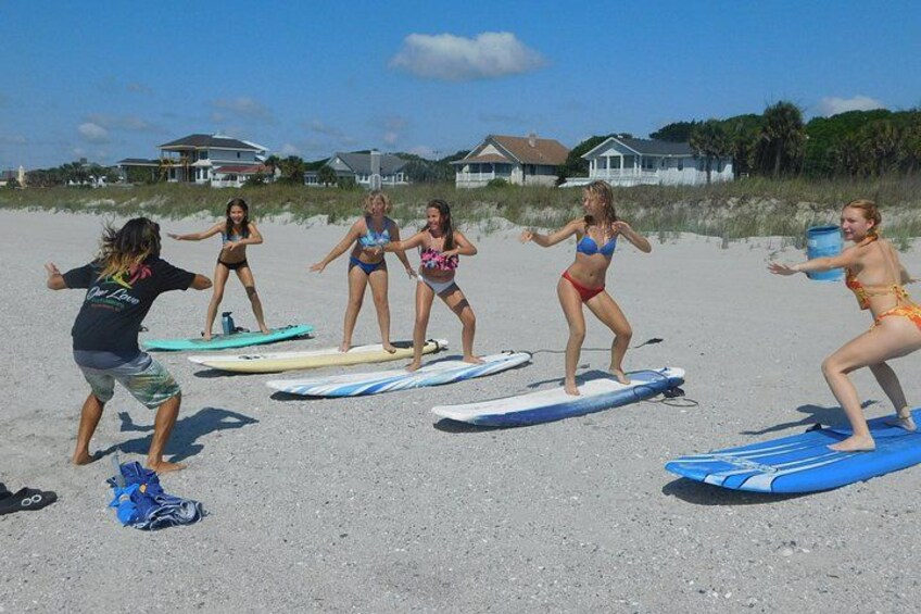 Un groupe de personnes fait de la planche à voile sur une plage de sable, avec des planches et sous un ciel dégagé. 1
