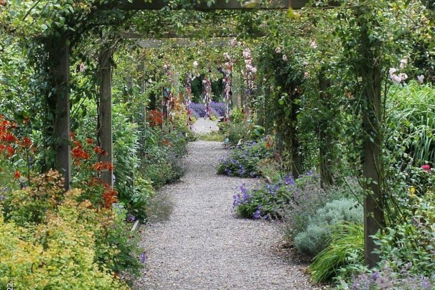 Een tuinpad met een pergola begroeid met klimplanten. 4