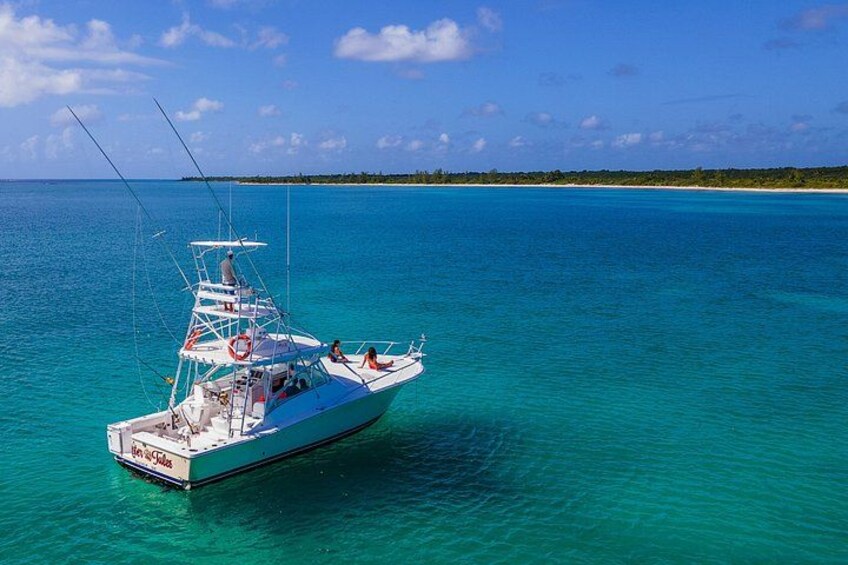 Un barco blanco con cabina y una persona en la cubierta, navegando sobre aguas turquesas bajo un cielo despejado. 1