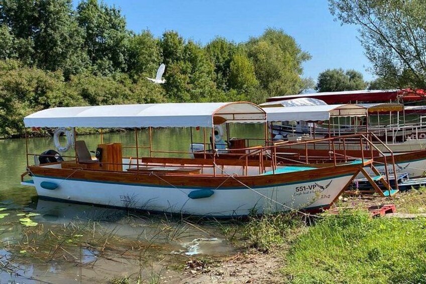 A wooden boat with a white canopy, docked near a riverbank with trees and a bird in flight. 3