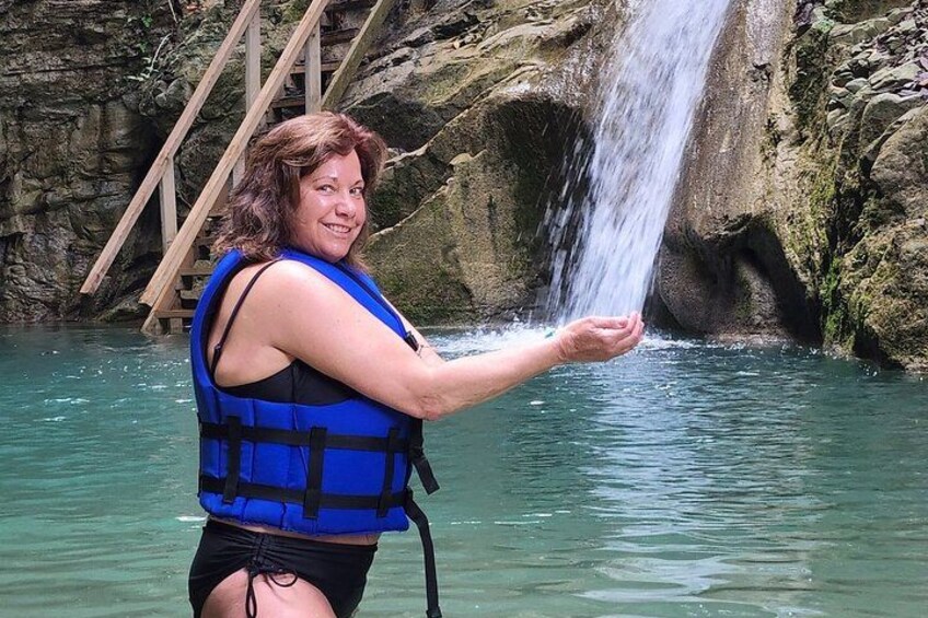 A person in a blue life jacket holding water from a waterfall. 4