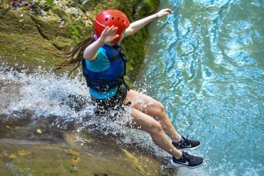 A person in a blue life jacket and red helmet jumping into a body of water. 2