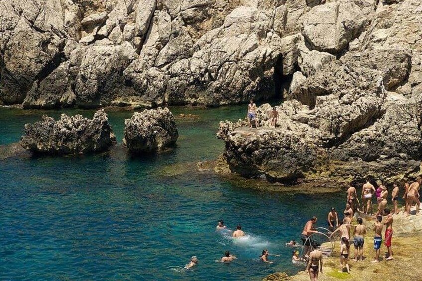 Una costa rocosa con gente nadando y caminando por la orilla. 3
