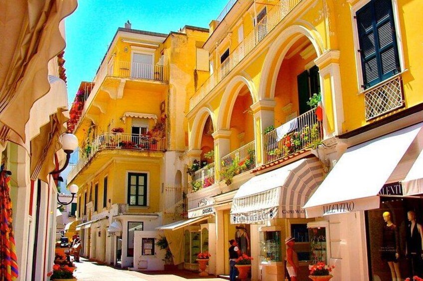 Una calle con edificios amarillos, balcones con plantas y comercios. 5