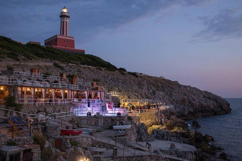 Zona costera con un faro, terreno rocoso y un restaurante frente al mar. 2