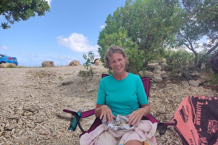 A person sitting on a chair outdoors with a rocky terrain and trees in the background. 4