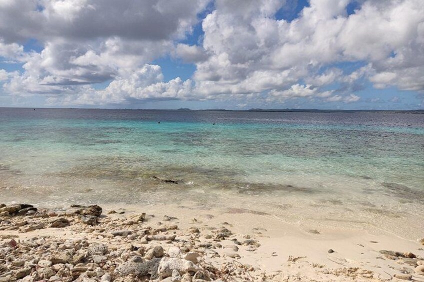 Una playa con agua turquesa cristalina, una orilla arenosa y rocas dispersas. 3