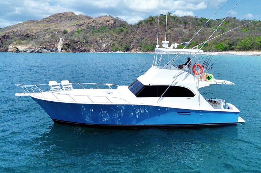 A blue and white boat on calm water with a rocky coastline and hills in the background. 1