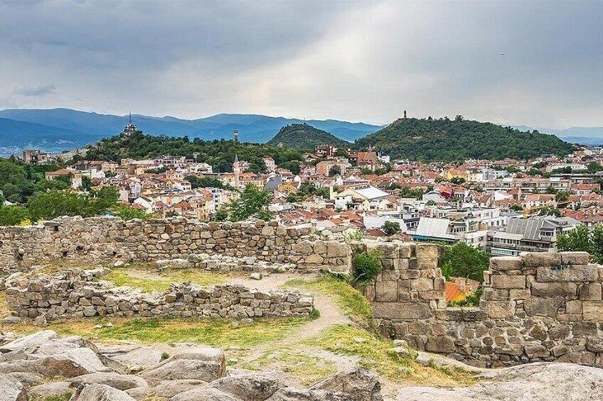 An ancient stone wall, a historic town with red-roofed buildings, and a hilltop with a tower. 2