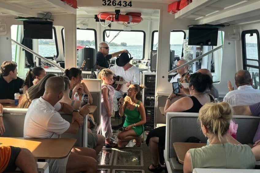 People on a boat, some seated, some standing, with a lifebuoy and a speaker visible. 1