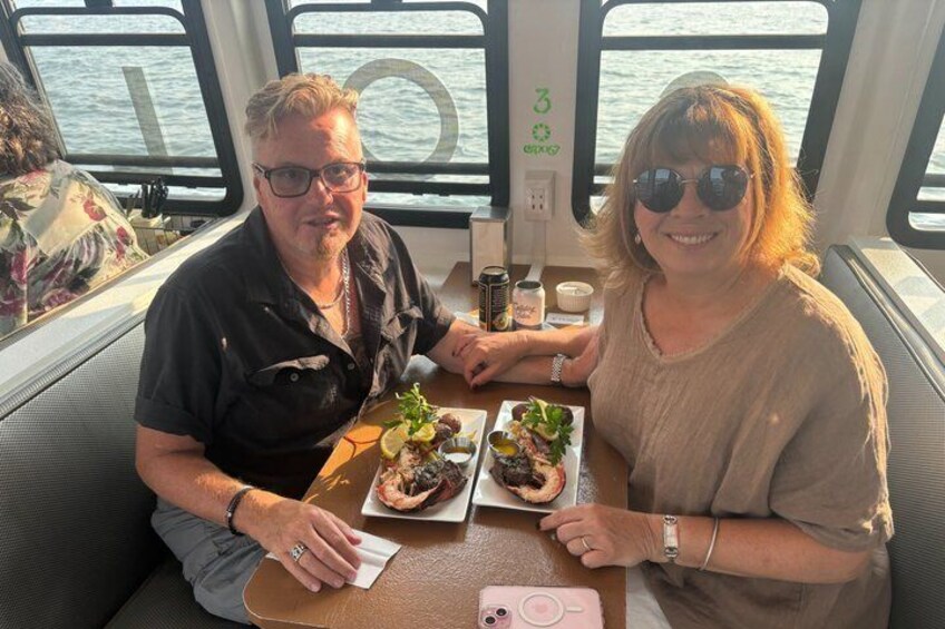 Dos personas sentadas en una mesa con comida y bebidas en un barco. 5