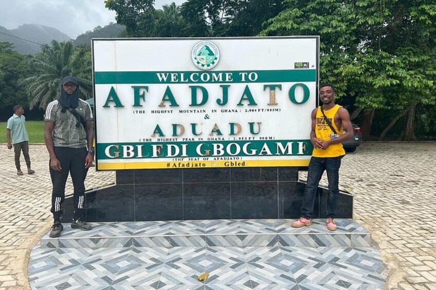 A welcome sign for Afadjato, Aduadu, with a mountain peak and a lake. 4