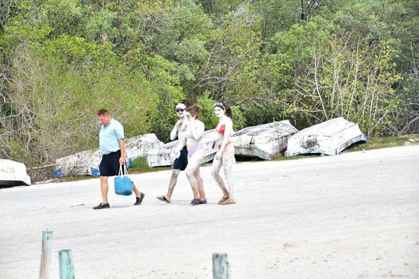 A sandy beach with people walking, a man carrying a blue bag, and large rocks in the background. 5