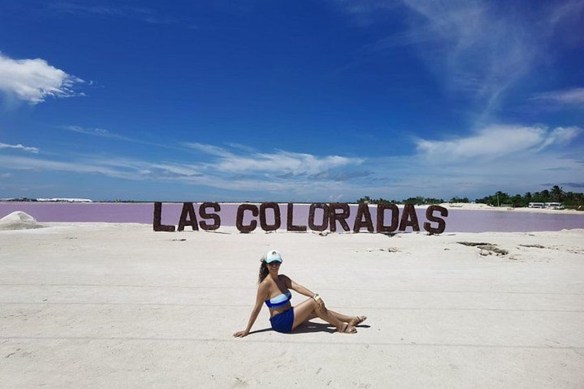 A person sitting on a sandy beach with a clear sky and the text 'LAS COLORADAS' in the background. 4