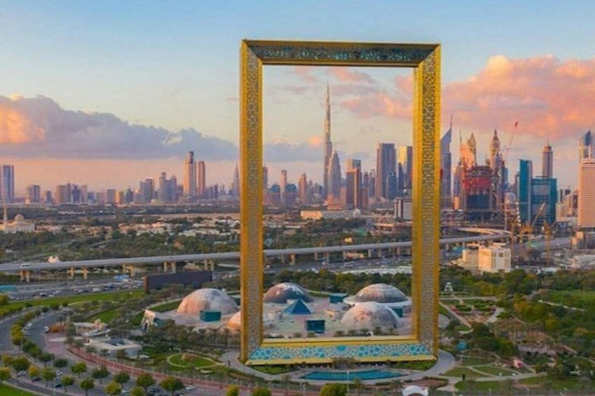 A cityscape with a prominent golden frame structure, modern skyscrapers, and a park with domed buildings. 1