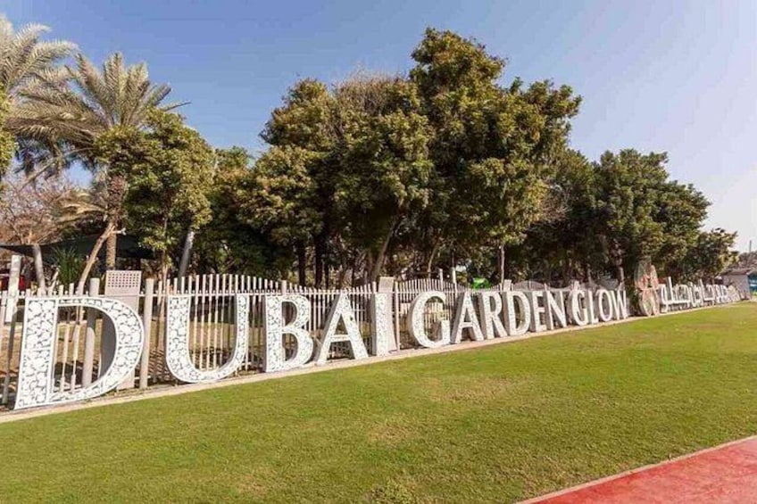 A sign with the words 'DUBAI GARDEN CITY' in large letters, surrounded by a white fence and palm trees. 2