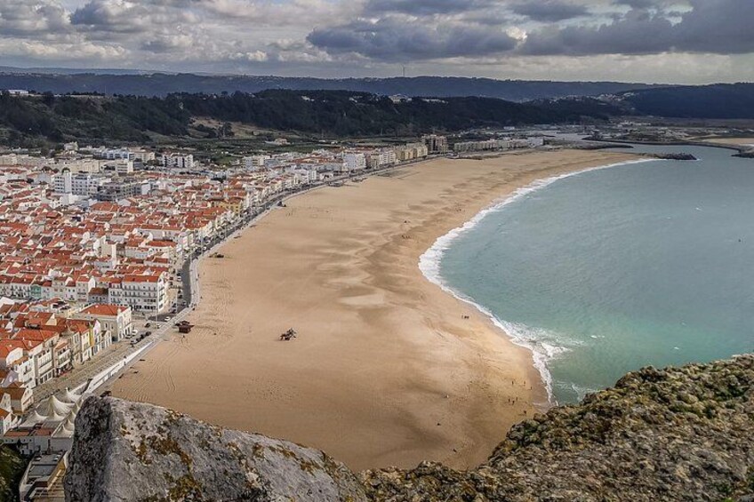 A coastal city with a wide sandy beach, a clear blue sea, and a hilly landscape in the background. 4
