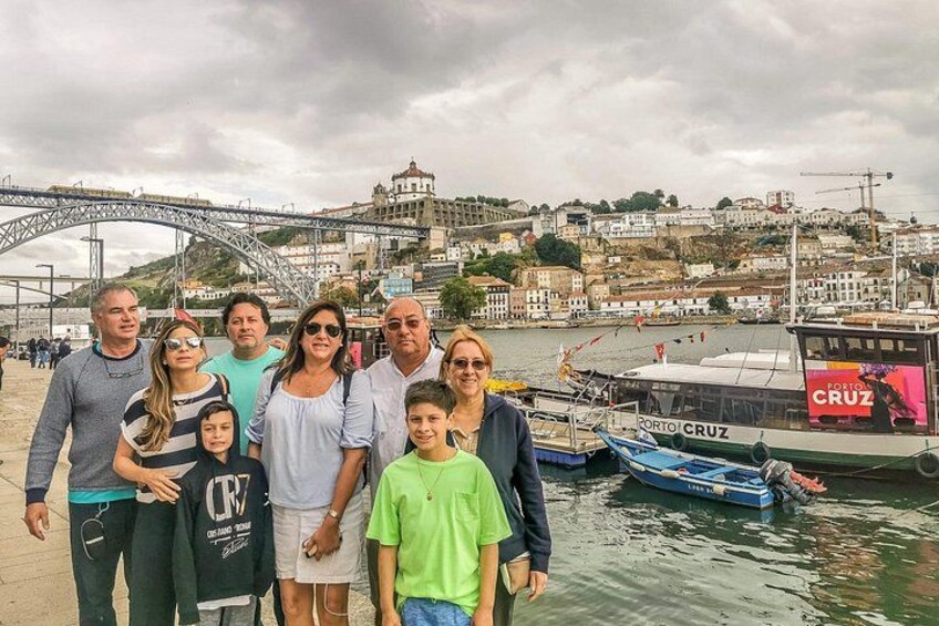 A group of people standing by a waterfront with a bridge and buildings in the background. 3